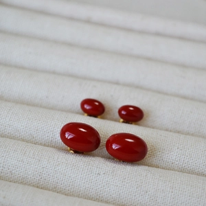 Detail of red enamel oval stud earrings in gold base on a beige fabric background