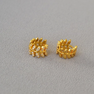 Detailed view of gold olive branch earrings with micro-set zircons on textured fabric