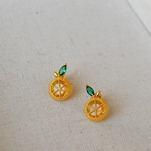 Macro shot of gold-plated orange earrings with yellow zirconia and green crystal leaves
