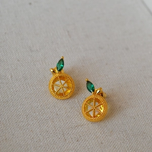 Macro shot of gold-plated lemon slice earrings with yellow zircons and green leaves