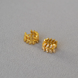 Gold olive branch hoop earrings with cubic zirconia leaves on a textured grey surface