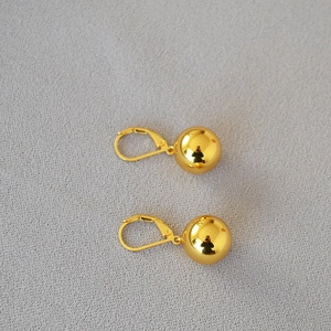 Macro detail of high-shine gold-plated brass ball earrings with secure leverback closures