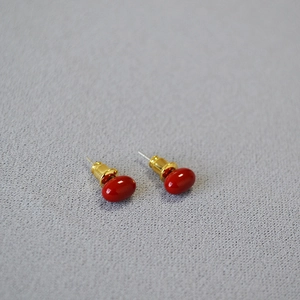 Close-up of red oval enamel stud earrings with polished gold metal base on gray background