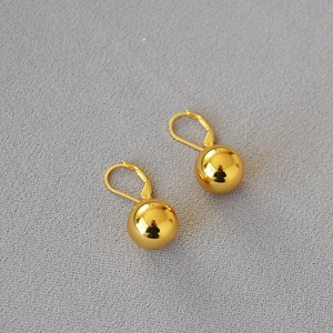 Minimalist polished gold hollow ball earrings with lever-back closure on grey fabric