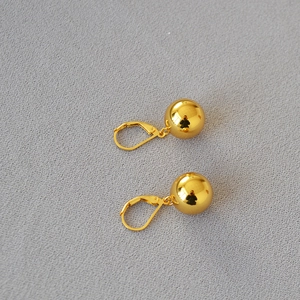 Macro view of polished golden hollow ball earrings with minimalist French leverback clasps