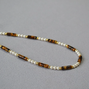 Macro shot of tiger eye beads, white pearls, and 18K gold beads on a retro necklace