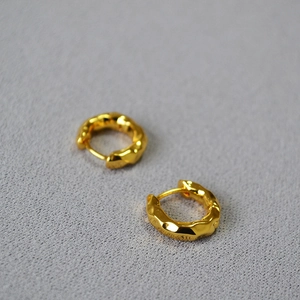 Macro shot of gold-plated brass hoop earrings featuring modern hammered texture