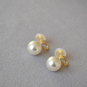 Détail de boucles d'oreilles perles blanches avec clips dorés et coussinets silicone