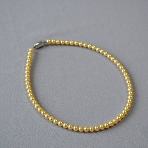 Détail d'un collier de perles dorées à haute brillance avec un fermoir magnétique argenté