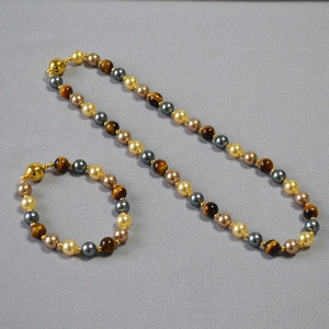 Close-up of tiger eye and pearl beaded necklace with magnetic gold clasp on grey background