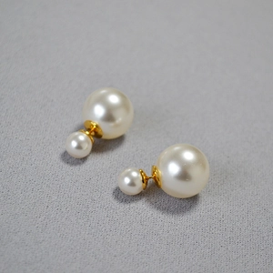 Macro detail of high-luster double pearl earrings with golden metal joinery on gray fabric