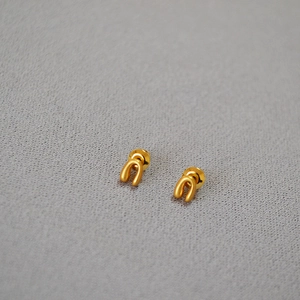 Macro shot of horseshoe stud earrings in matte gold finish on grey textured fabric