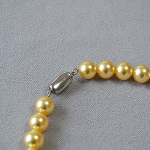 Gros plan d'un collier de perles dorées avec un fermoir cylindrique métallique élégant