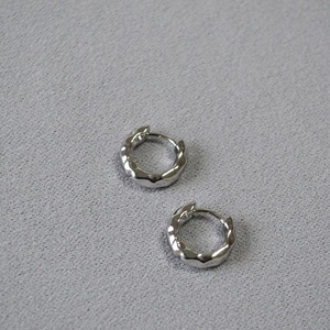 Detailed view of silver huggie earrings with unique hammered wavy texture and high polish