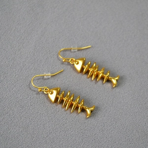 Macro detail of gold-plated fish bone earrings with matte texture on grey fabric