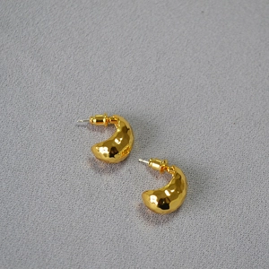 Macro detail of gold-plated crescent earrings showing unique hammered texture and shiny finish