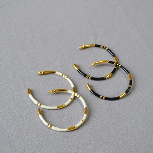 Detail view of large C-shaped bamboo-style enamel hoop earrings in black and white gold finish