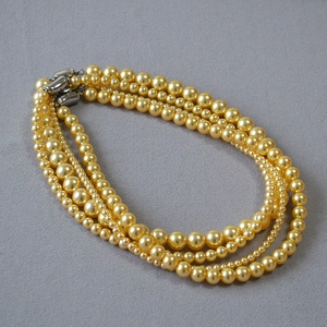 Détail d'un collier de perles dorées multicouches avec des boucles en argent et éclat chic