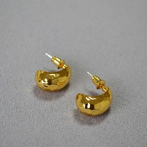 Macro shot of gold-plated crescent stud earrings with hammered texture on grey fabric