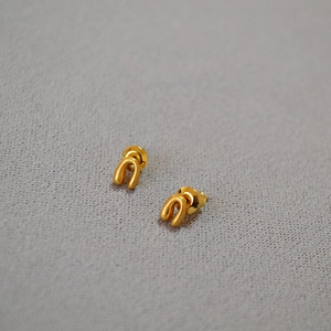 Minimalist matte gold horseshoe stud earrings with textured finish on gray fabric