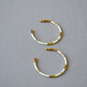 Macro detail of gold-plated bamboo oversized hoop earrings with white enamel finish