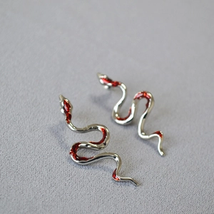 Detailed close-up of snake earrings with silver finish and vibrant red enamel inlay
