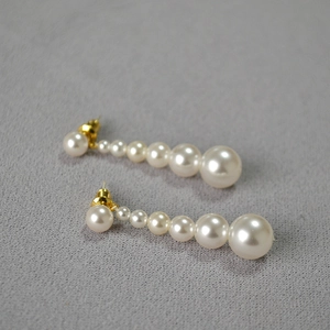 Détail de longues boucles d'oreilles perles dégradées avec tiges dorées sur tissu gris