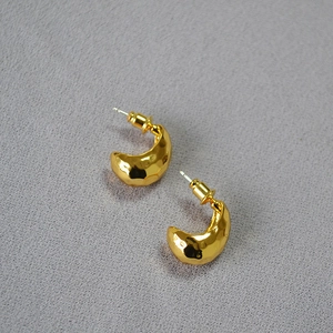 Close-up of golden C-shape earrings with vintage hammered texture and metallic finish