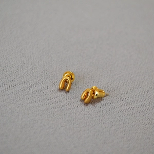 Macro detail of golden U-shaped horseshoe earrings on light textured fabric background