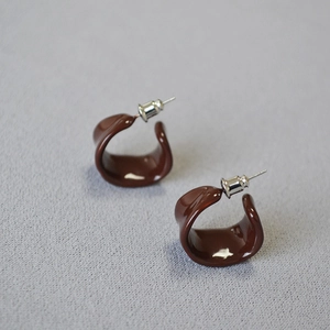 Close-up of burgundy enamel C-shaped stud earrings with silver pins and metal backs