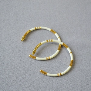 Close-up of gold-plated bamboo hoop earrings with ivory enamel details on textured fabric