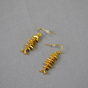 Detailed view of vintage gold-plated brass fishbone earrings on grey textured fabric