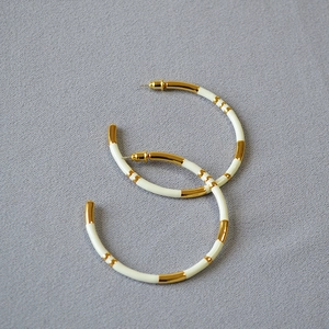 Detail of oversized gold-plated bamboo hoop earrings with white enamel finish