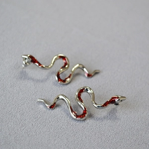 Futuristic silver snake earrings with deep red stone inlays on textured background