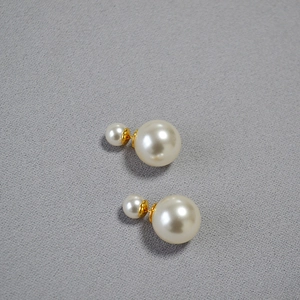 Detail of double pearl earrings featuring 12mm and 8mm white pearls with gold pins