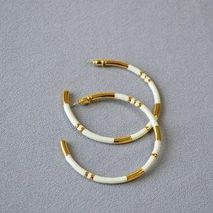 Close-up of gold-plated bamboo-joint hoop earrings with white enamel detail and silver posts