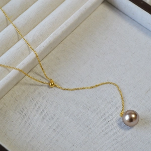 Détail d'un pendentif perle champagne sur une fine chaîne dorée posée sur un plateau en lin