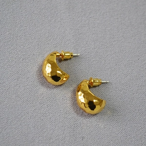 Macro detail of golden crescent earrings featuring a unique hammered texture finish