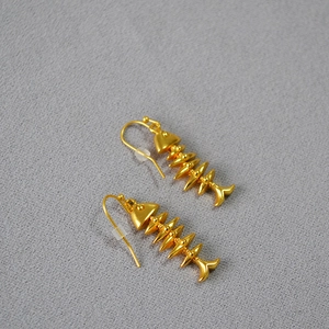Macro detail of matte gold vintage fishbone earrings on a grey textured background