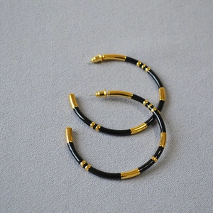 Detailed shot of large gold-plated bamboo-style hoop earrings with black enamel sections