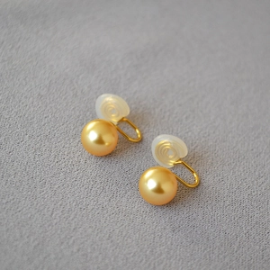 Détails macro de boucles d'oreilles clips perles dorées avec attaches en U et coussinets