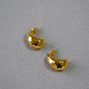 Macro view of golden hammered texture C-shape earrings with artistic curved surface