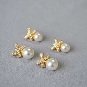 Detail of elegant brass X-cross earrings with inlaid zircons and hanging round pearls
