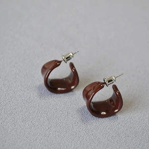 Macro shot of burgundy red enamel C-shaped stud earrings on light gray textured fabric