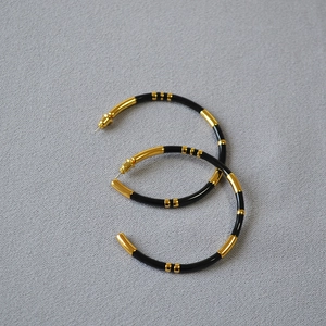 Detailed view of oversized gold-plated bamboo hoop earrings with black enamel accents