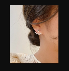 Close-up of elegant gold heart stud earrings with five pearls surrounding the earlobe