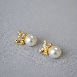 Macro detail of X-shaped gold-plated pearl earrings with inlaid zircon on gray texture