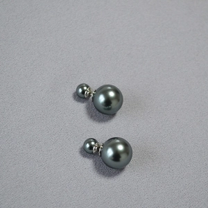 Detailed view of dark grey double pearl earrings with metallic luster on grey fabric