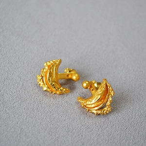 Detail of gold crescent earrings with vintage hammered texture on gray fabric