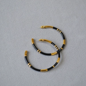 Detailed shot of large C-shaped bamboo hoop earrings with gold plating and black enamel